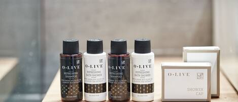 Four O.LIVE products: two bottles of refreshing shampoo and two shower caps, all labeled for all skin types.