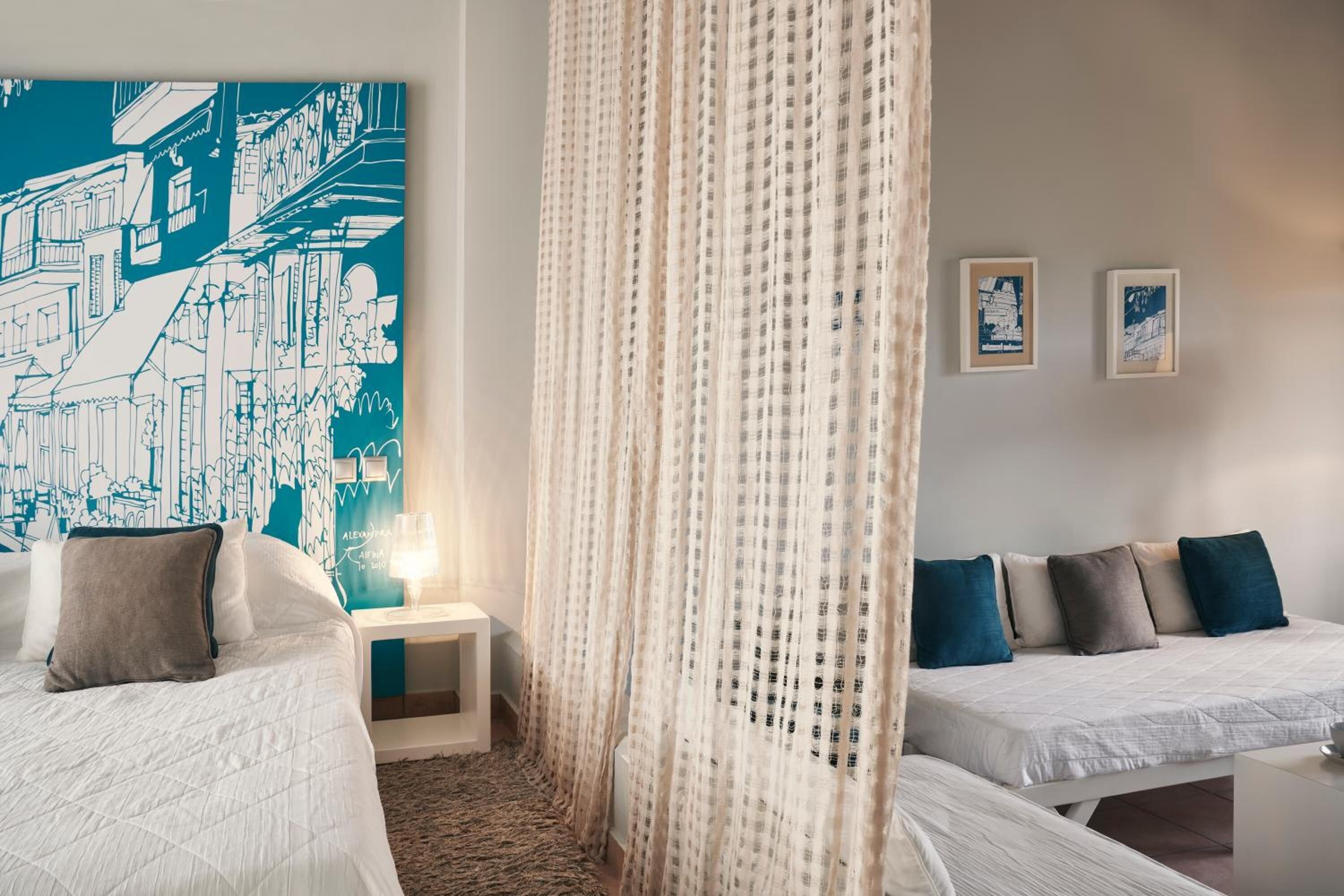A hotel room with two beds, a large wall mural, a bedside table with a lamp, and a curtain.