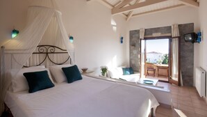 A bedroom with a canopy bed, a stone wall, a television, and a view of the outdoors. - Angelina Aegina Boutique Escape (Aegina)