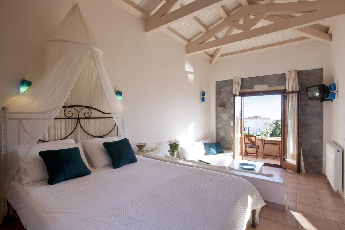 A bedroom with a canopy bed, a stone wall, a television, and a view of the outdoors.