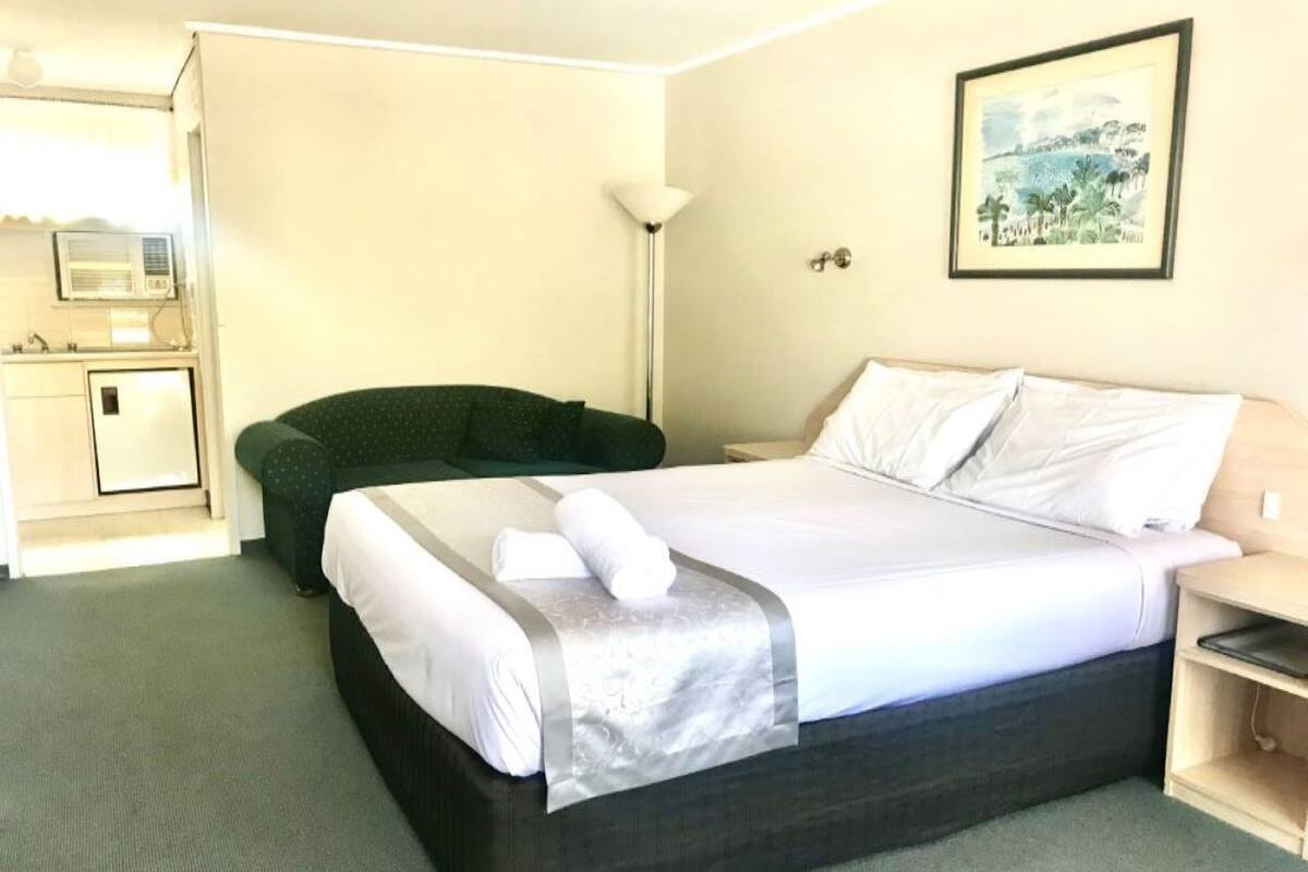 Une chambre d’hôtel avec un lit, un bureau, une chaise, une lampe et un tableau au mur.