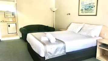 A hotel room with a bed, a desk, a chair, a lamp, and a picture on the wall.