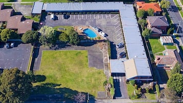 Vista aérea de un edificio con estacionamiento, piscina y zonas verdes circundantes.