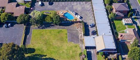 Vista aérea de un edificio con estacionamiento, piscina y zonas verdes circundantes.