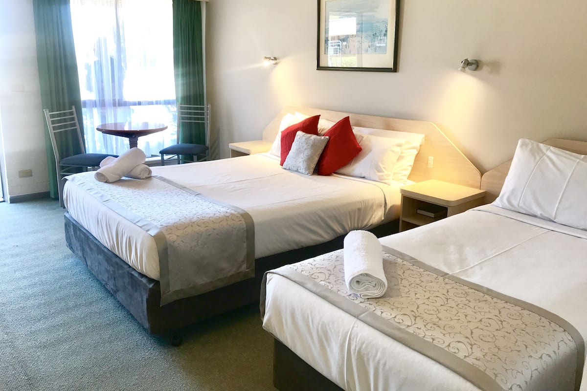 Une chambre d’hôtel avec deux lits, une petite table, une chaise et une fenêtre avec des rideaux.