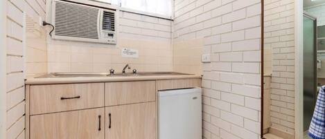 Una cocina compacta con pileta, armarios, un refrigerador pequeño y un equipo de aire acondicionado.