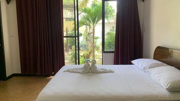 A hotel room with a bed, a window with curtains, and a view of a garden.