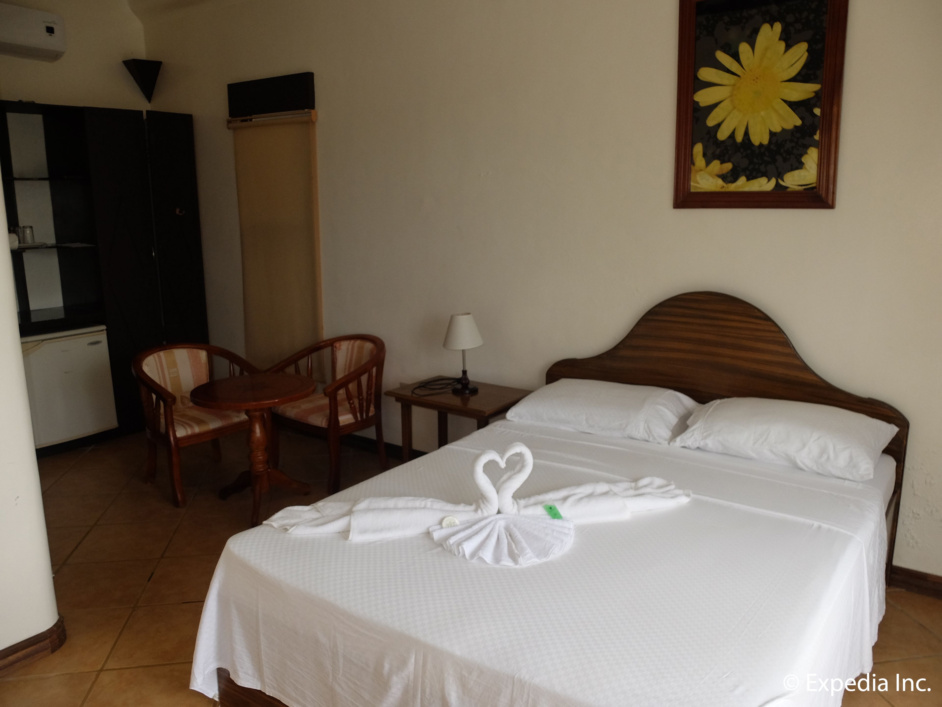 Habitación de hotel con cama, escritorio, silla, lámpara y un cuadro en la pared.
