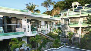 A multi-story hotel with a green and white exterior, a central staircase, and outdoor seating areas. - Turtle Inn Resort (Boracay Island)
