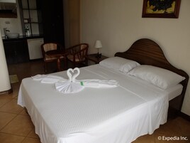 Una habitación de hotel con una cama bien hecha, cabecera de madera, comedor con sillas y una cocina al fondo.