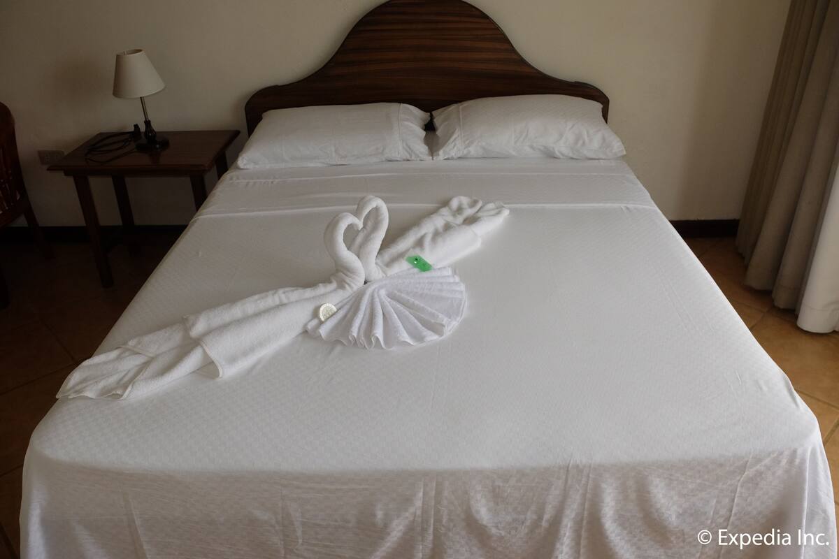 A hotel room with a neatly made bed, a nightstand with a lamp, and a window with curtains.