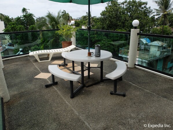 A round table with benches, a potted plant, and a table lamp on a balcony with a glass railing and palm trees in the background. - Turtle Inn Resort (Boracay Island)