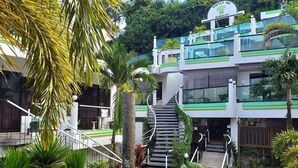 A modern building with a curved staircase leading to a green-roofed entrance, surrounded by lush tropical plants. - Turtle Inn Resort (Boracay Island)