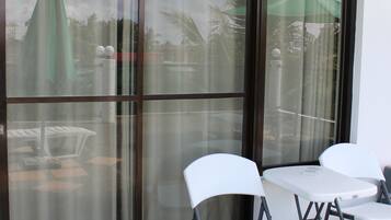 Un balcon avec une porte-fenêtre coulissante, des chaises blanches et une petite table.