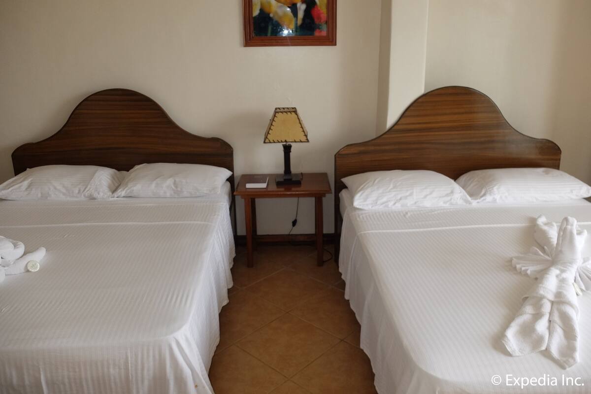 A hotel room with two beds, a nightstand with a lamp, and a painting on the wall.