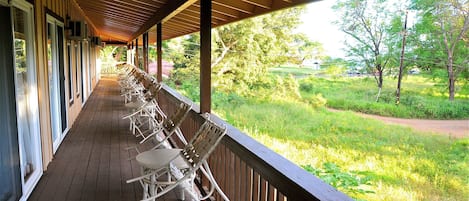 A covered porch with white chairs and a view of a grassy area with trees.