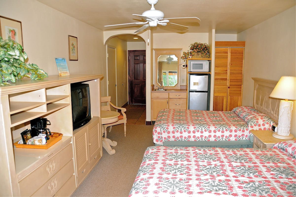 A hotel room with two beds, a television, a microwave, a refrigerator, a desk, and a ceiling fan.