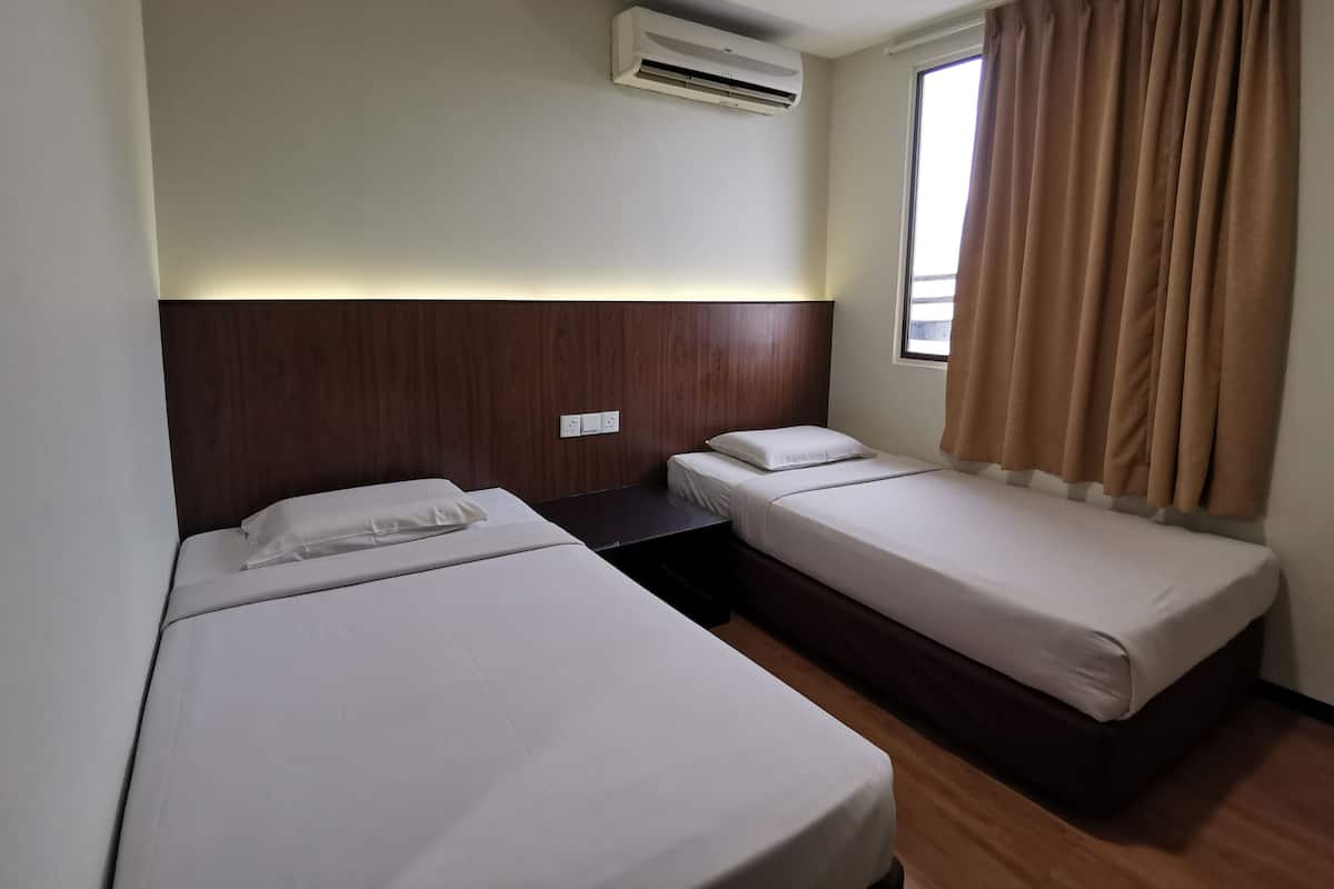 A hotel room with two single beds, a wooden headboard, an air conditioning unit, and a window with curtains.