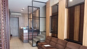 A modern interior with a brown sofa, a reception desk, and a staircase with a metal railing. - Hotel Holiday (Kota Kinabalu)