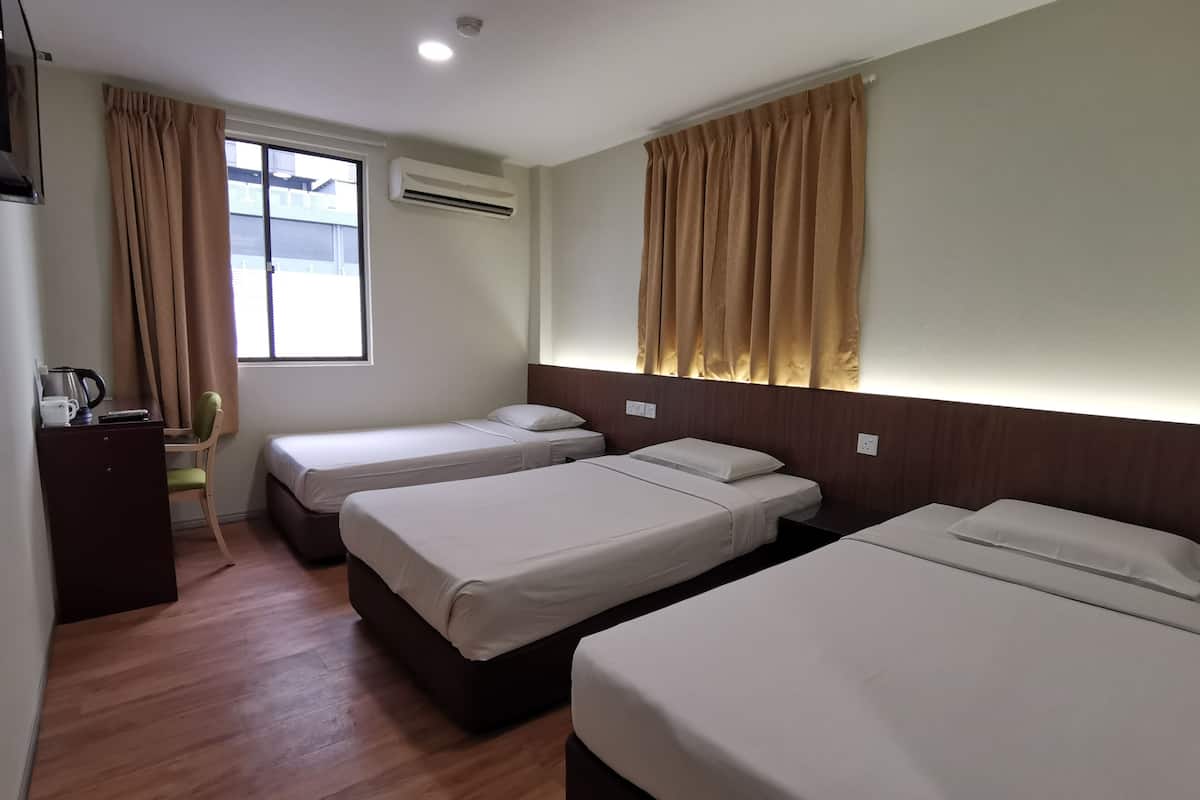 A hotel room with three single beds, a desk with a chair, an air conditioning unit, and a window with curtains.