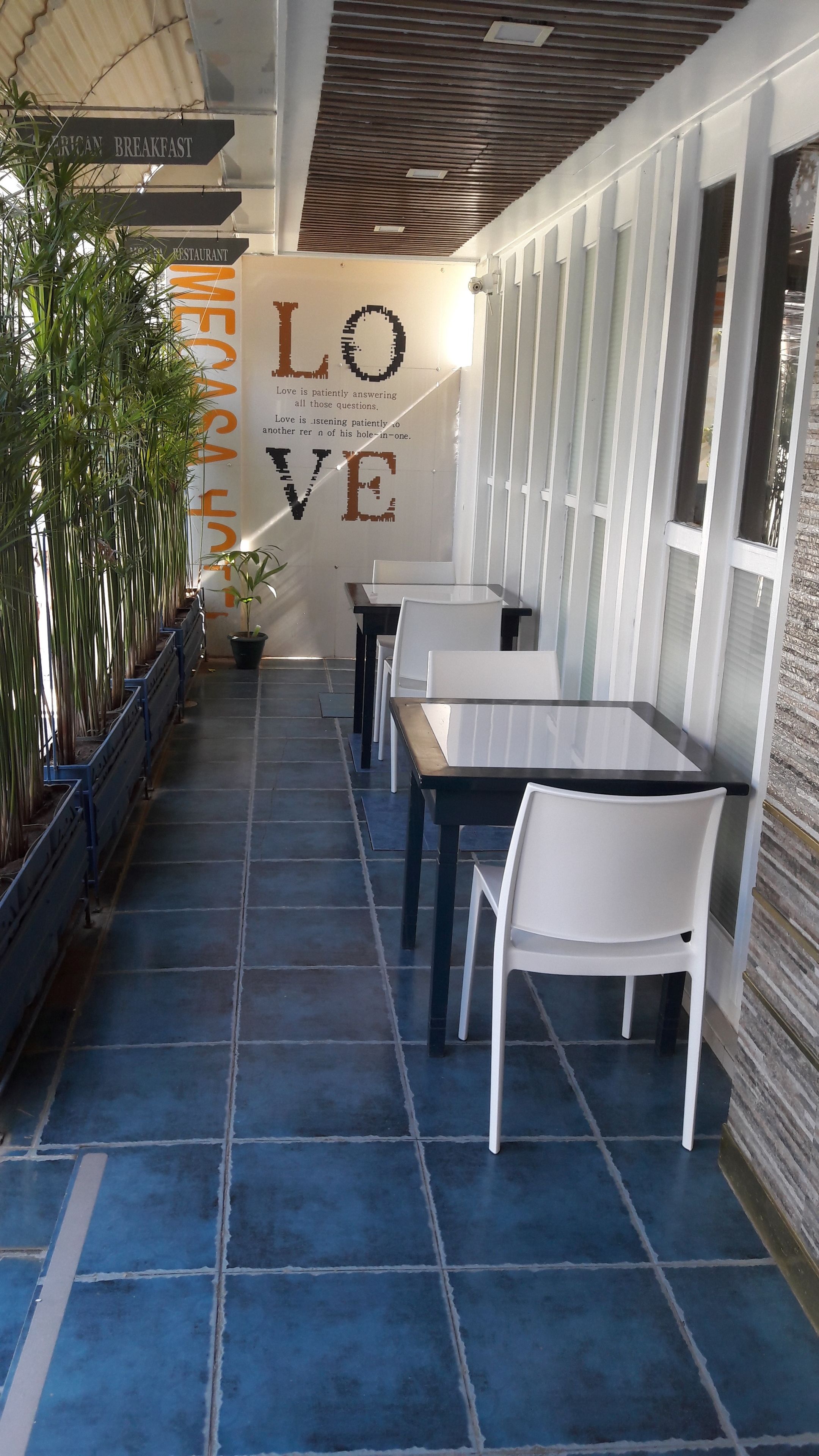 A restaurant with a blue-tiled floor, white tables and chairs, and a wall with a 'LOVE' sign and a quote.