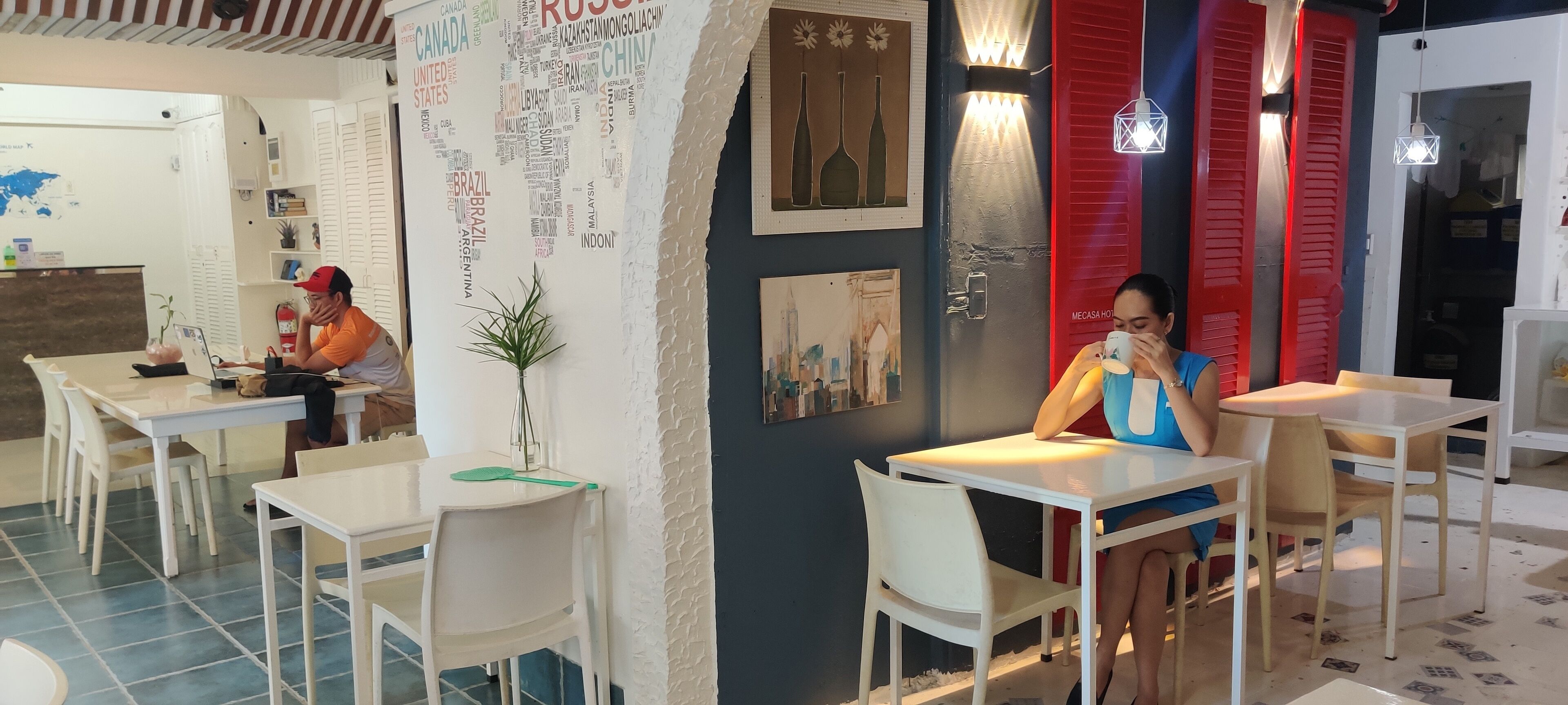 A restaurant with white tables and chairs, red doors, and a wall with country names.