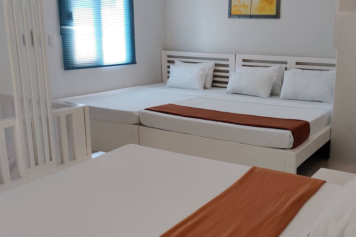 Hotellihuone, jossa on sänky, pieni pöytä, tuoli ja ikkuna, jossa on sälekaihtimet.