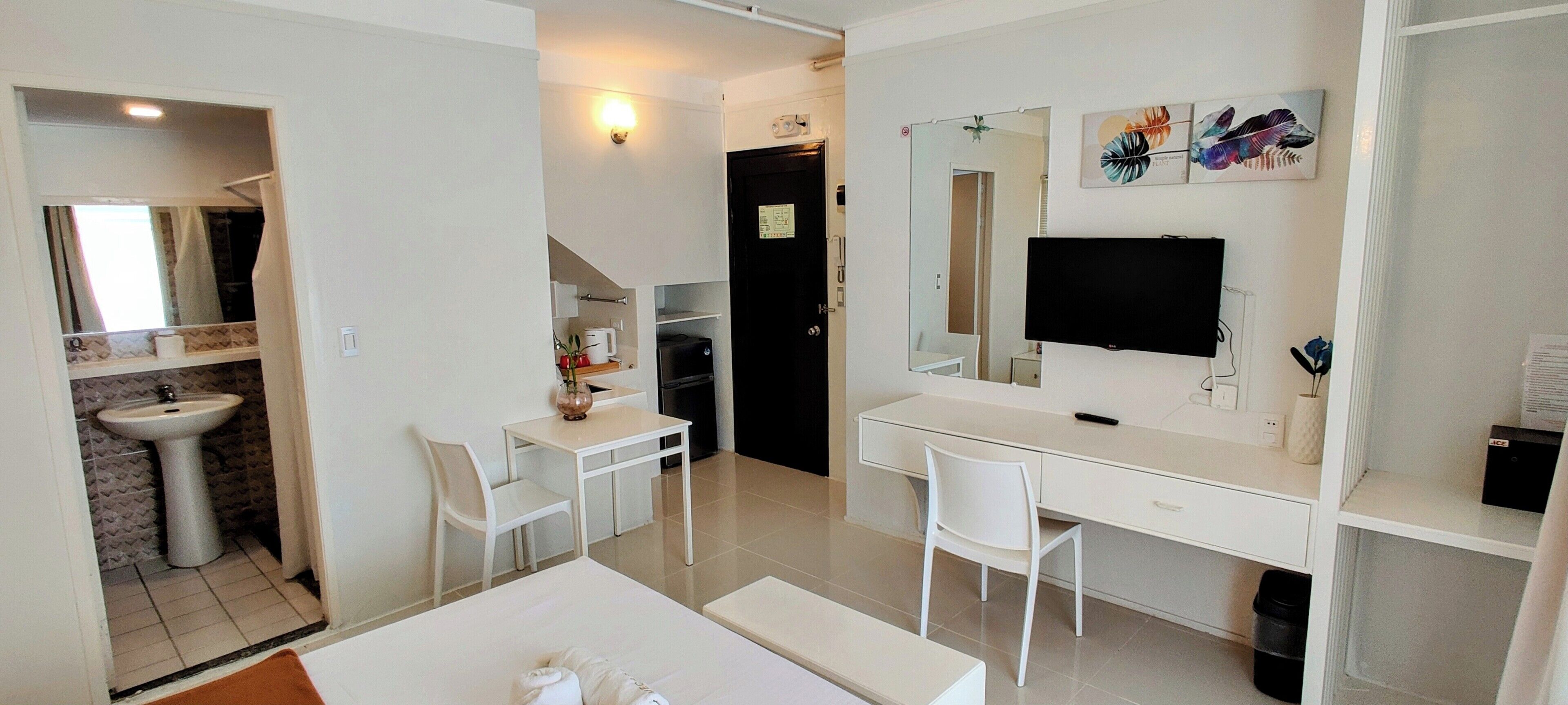 A hotel room with a bed, a desk, a chair, a TV, a mirror, a sink, and a door leading to a bathroom.