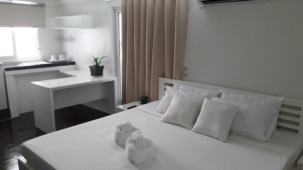A hotel room with a bed, a desk, a sink, and a potted plant.