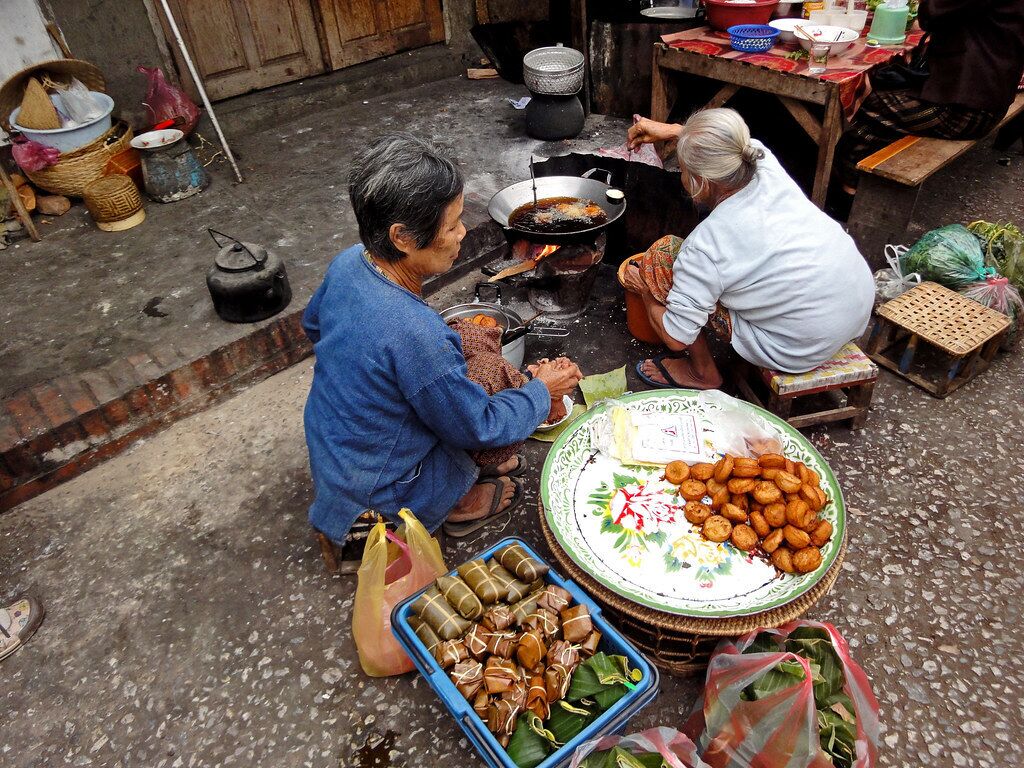 A street food vendor cooking outdoors with a variety of food items and cooking utensils visible.