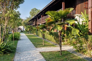 Un sendero que lleva a un edificio de madera con balcones, rodeado de plantas tropicales y un cielo despejado.
