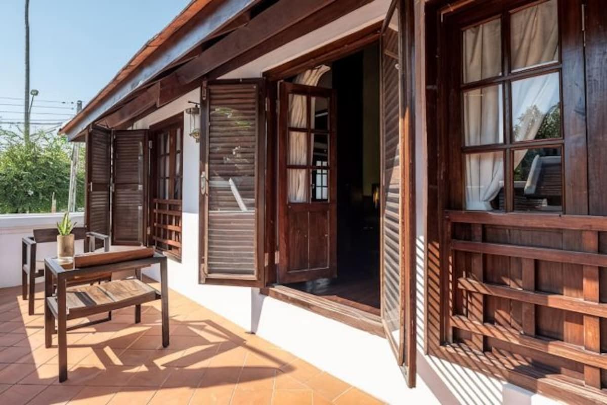 Un edificio de madera con puertas y ventanas abiertas, una banca y una planta en maceta.