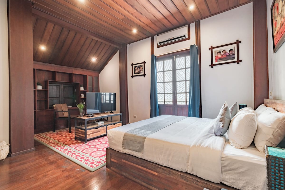 Une chambre avec un plafond en bois, un lit avec une literie blanche, un bureau avec une chaise et un téléviseur.
