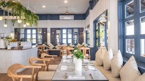 Un restaurante con sillas de madera, una mesa larga con servilletas blancas y plantas colgantes.