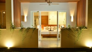 Un dormitorio moderno con una cama centrada en la habitación, un ventilador de techo arriba y una puerta de cristal que da al baño.