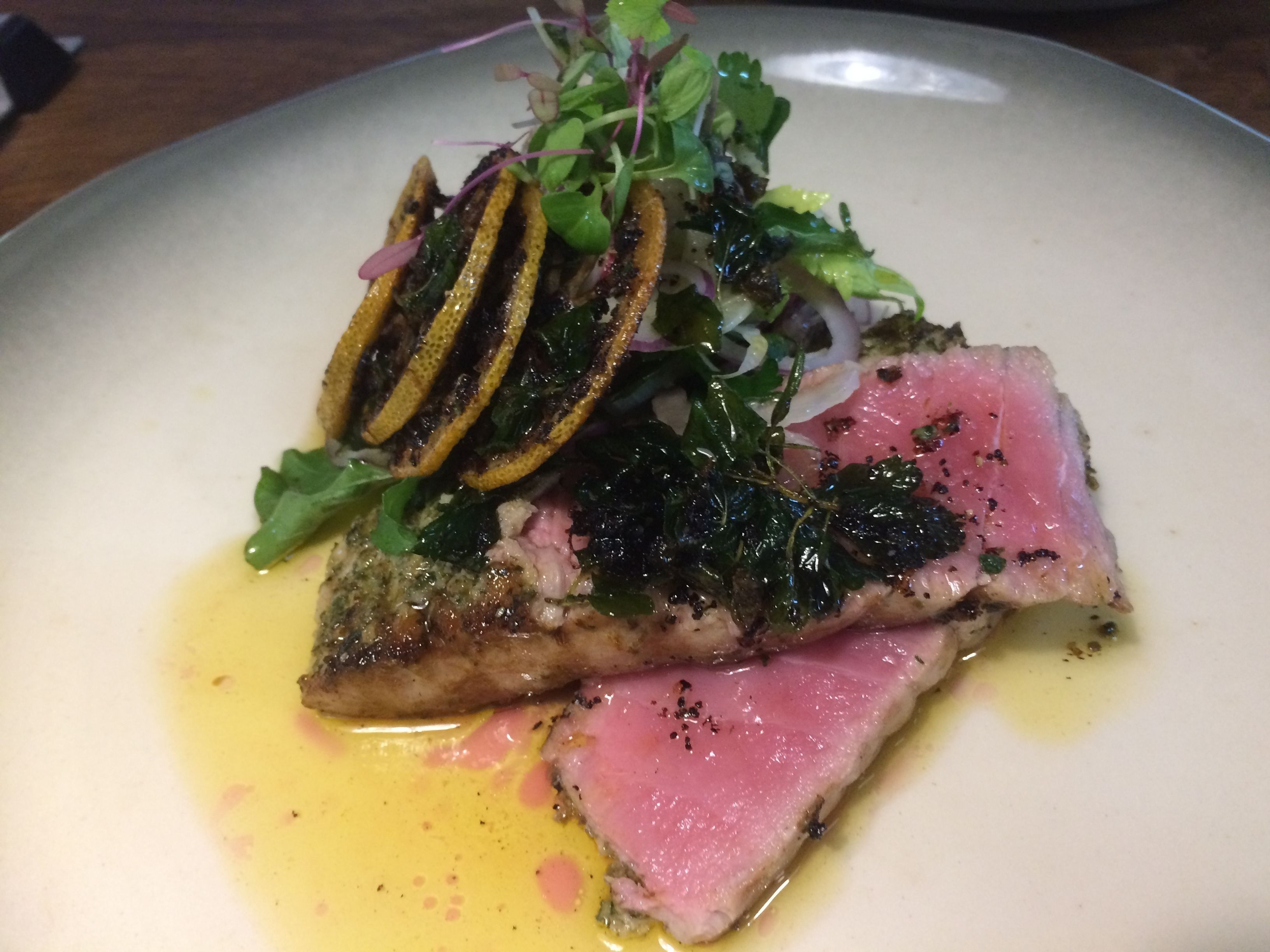 A plate of food with a piece of meat, greens, and lemon slices.