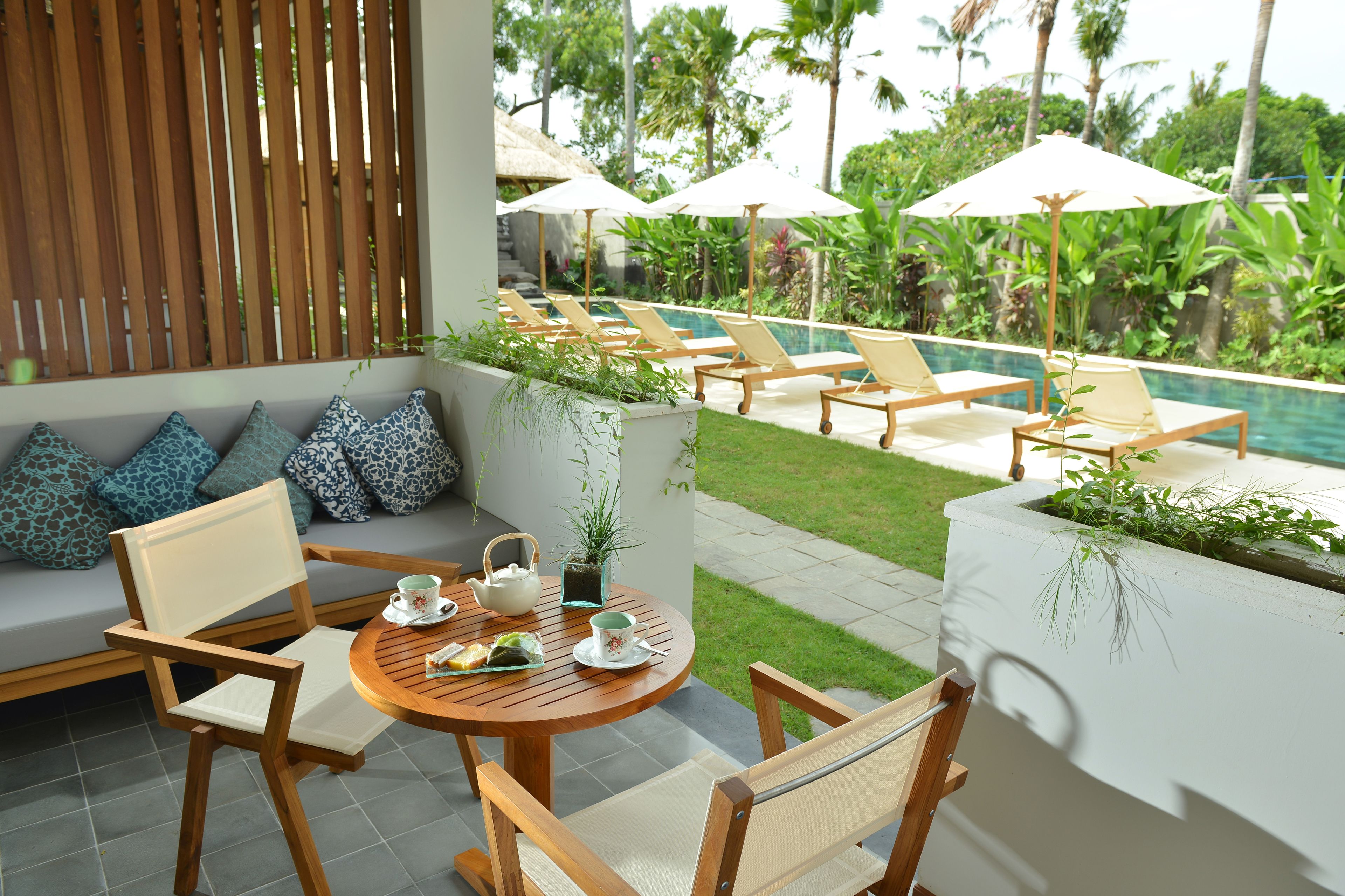 Eine Terrasse mit Pool, Liegestühlen, einem Tisch mit Teekanne und einer Couch mit gemusterten Kissen.