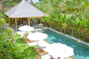 Relax by the serene pool surrounded by lush tropical plants and a thatched-roof gazebo.