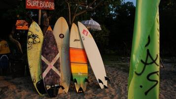 Tablas de surf alineadas en una playa arenosa, con un cartel que dice 'FOR RENT SURFBOARD'.