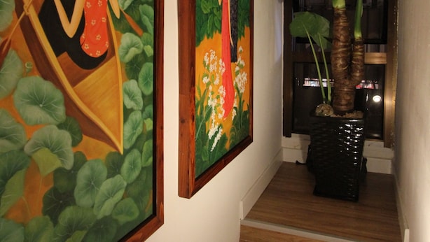 Un couloir orné de deux grands tableaux, d’une plante en pot et d’un escalier en bois.