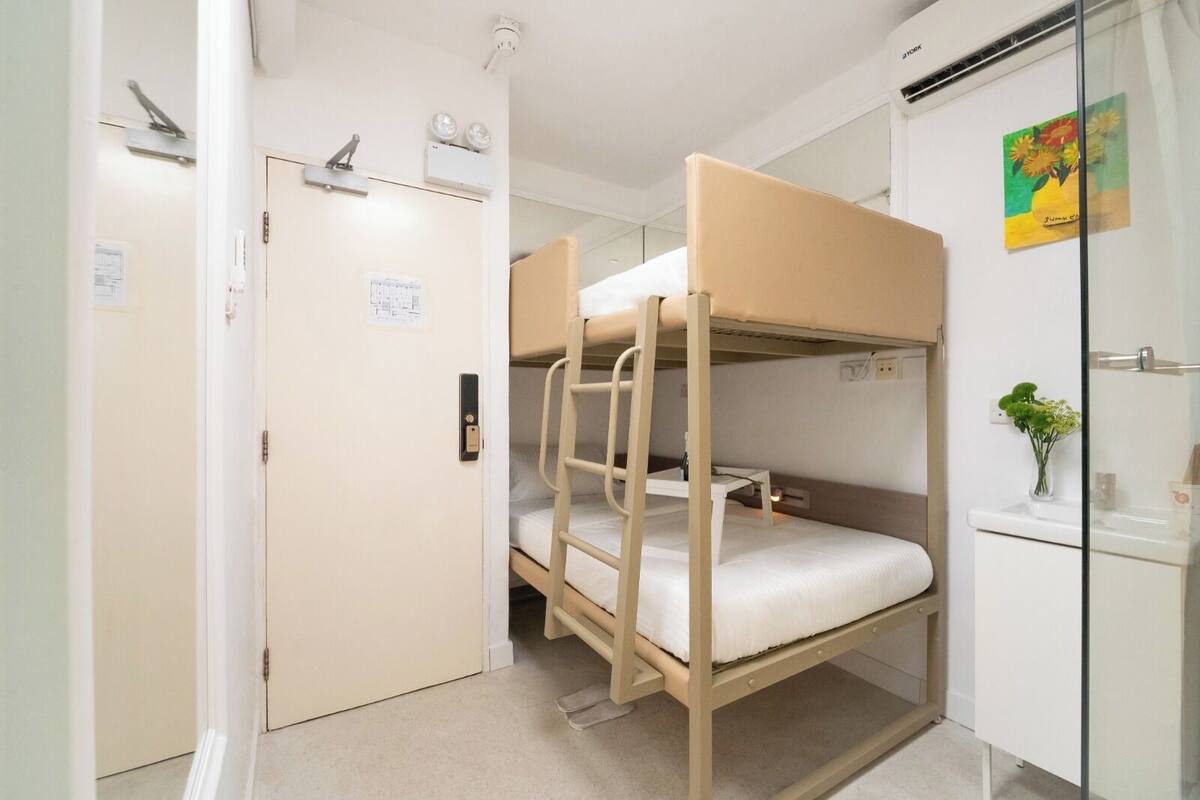 A bunk bed room with a white door, a small desk with a vase of flowers, and a wall-mounted air conditioner.