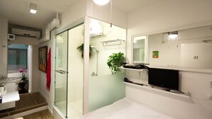 Une salle de bain moderne dotée d’une douche à parois de verre, d’un téléviseur fixé au mur et d’un lavabo avec un miroir.