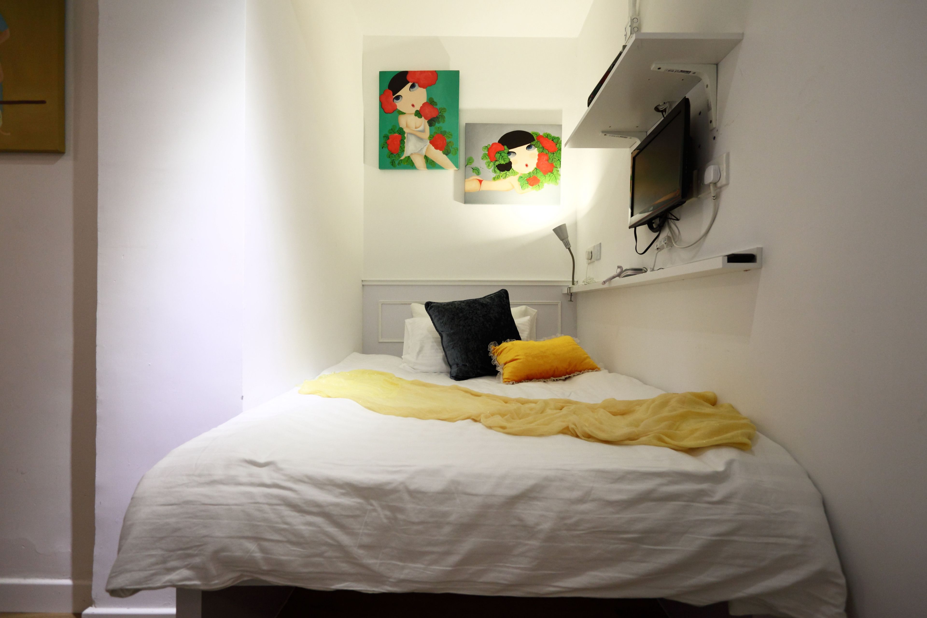 Ein Schlafzimmer mit einem Bett, weißen Wänden, einem an der Wand befestigten Fernseher und zwei Bildern.