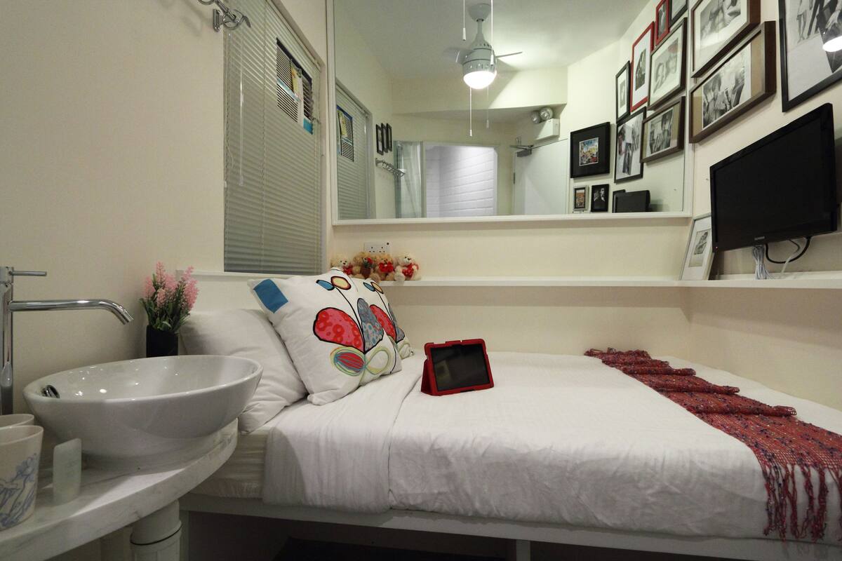 A bedroom with a white bed, a red tablet, a white sink, and a mirror.