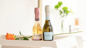 Deux bouteilles de vin sur une surface blanche, avec une rose et des feuilles vertes en arrière-plan.