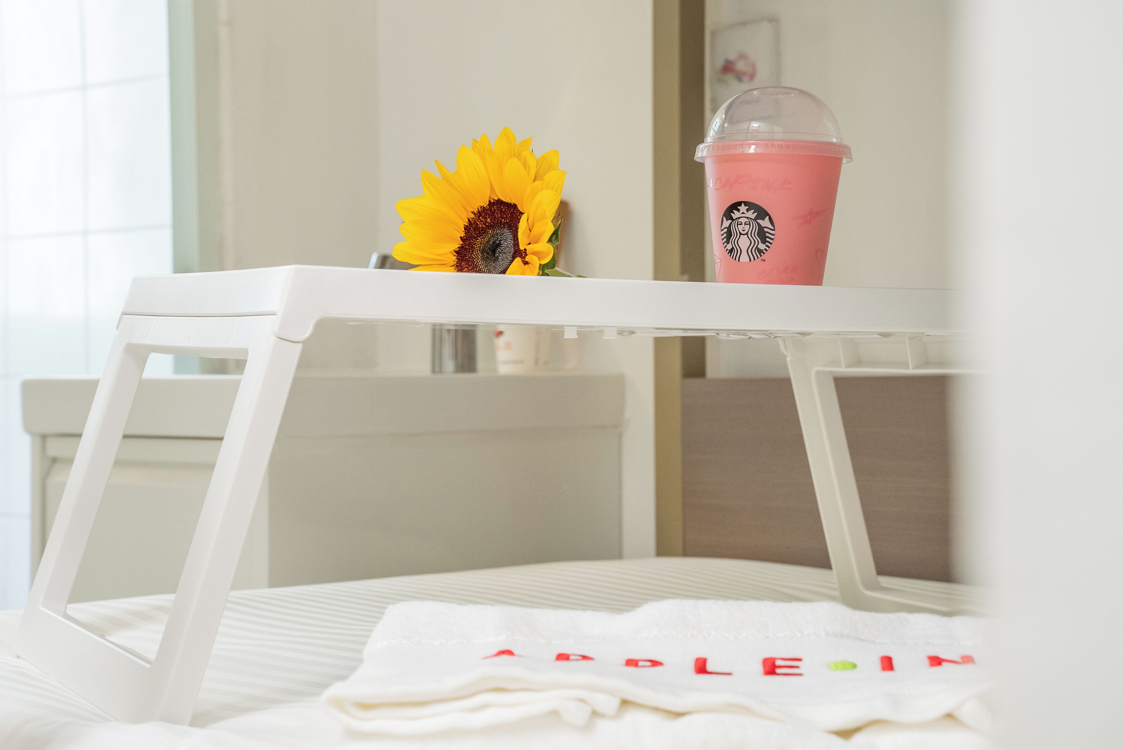 Una silla blanca con un paño blanco doblado encima, una taza rosa de Starbucks y un girasol.