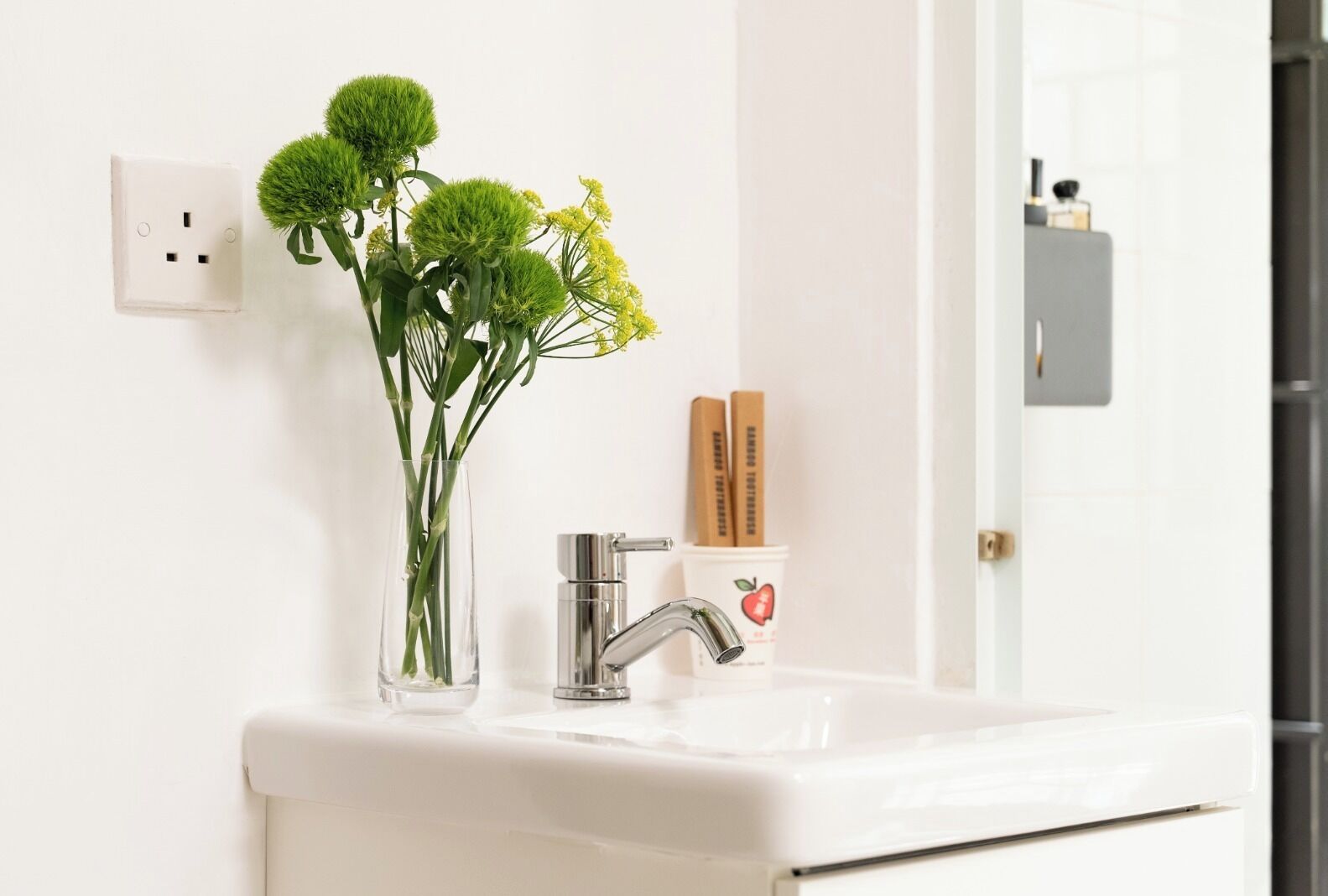 A bathroom with a white sink, a modern faucet, and a vase with green plants.