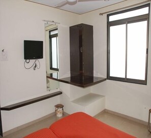 A room with a bed, a TV mounted on the wall, a window, and a small table with a lamp. - Skyway Inn (Mumbai)