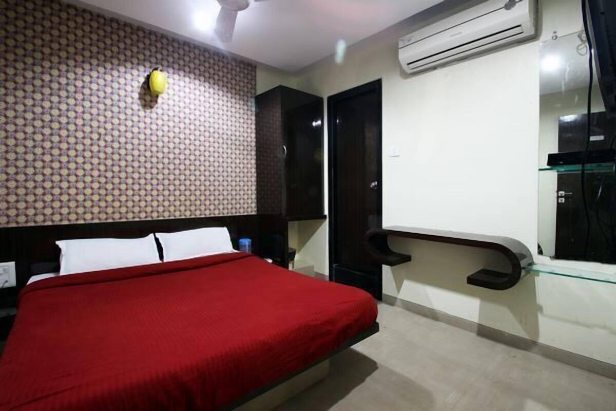 A hotel room with a bed, a wall-mounted air conditioner, and a glass shelf.