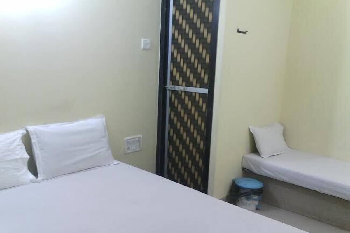 A small, single-room accommodation with two beds, a blue trash bin, and a patterned door.